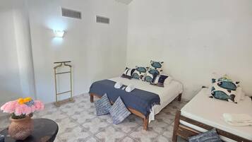 A room with two beds, a small table with a vase of flowers, and patterned floor tiles.