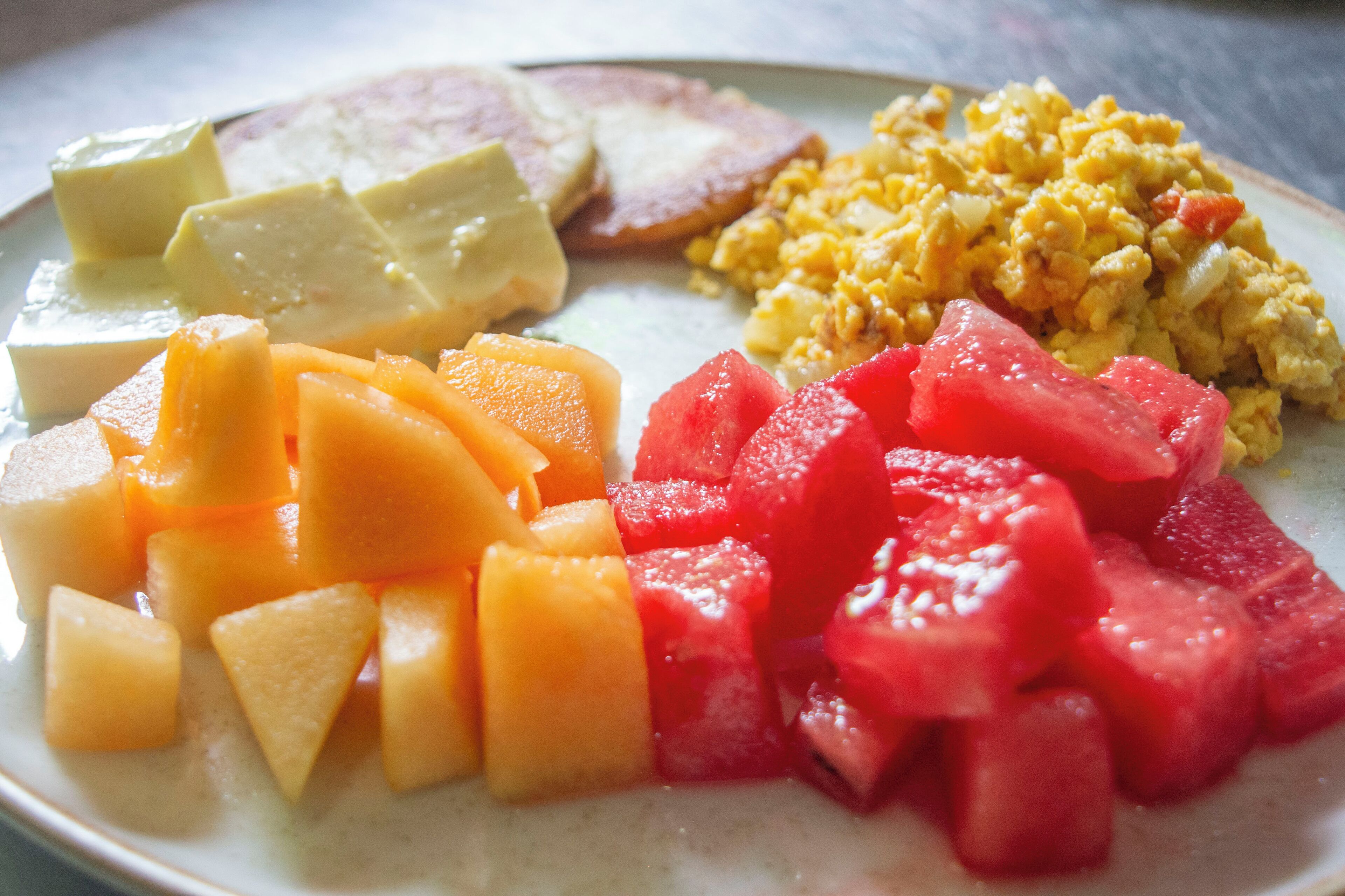 Ein Teller mit verschiedenen Speisen, darunter Käse, Rührei und gewürfelten Früchten.