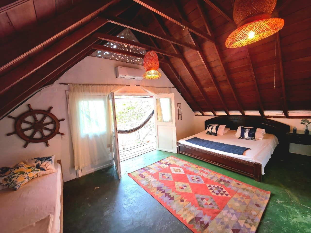 Un dormitorio acogedor en el ático con techo de madera, una hamaca, una cama con alfombra colorida y una decoración con timón de barco.