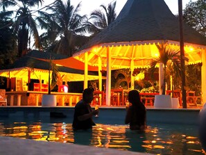 A pool area with a covered seating area and palm trees. - Hotel Isla Azul  (Rosario Islands)