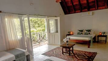 A room with a bed, a small table with a vase, a patterned rug, and a balcony with a railing.