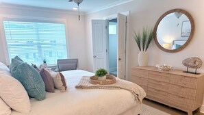 Ein Schlafzimmer mit Bett, Nachttisch, Kommode, Spiegel und einem Fenster mit Jalousien.