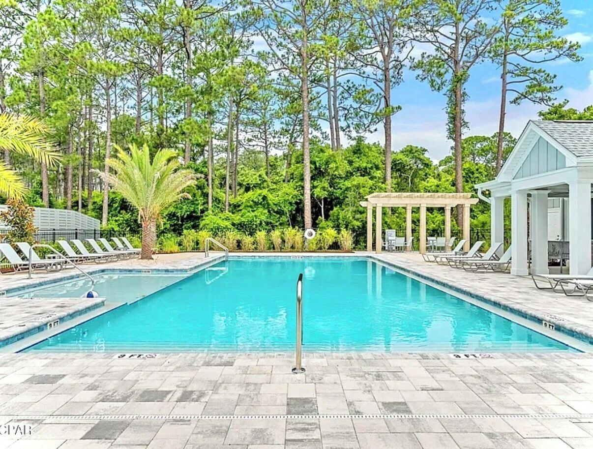 A rectangular swimming pool with a clear blue water, surrounded by lounge chairs and a covered seating area.