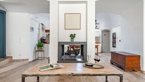 A spacious living area with a fireplace, a dining table with a book and wine glass, and a view of the kitchen. - Dimora San Michele - Exclusive Villa among Trulli, with Private Pool (Puglia)