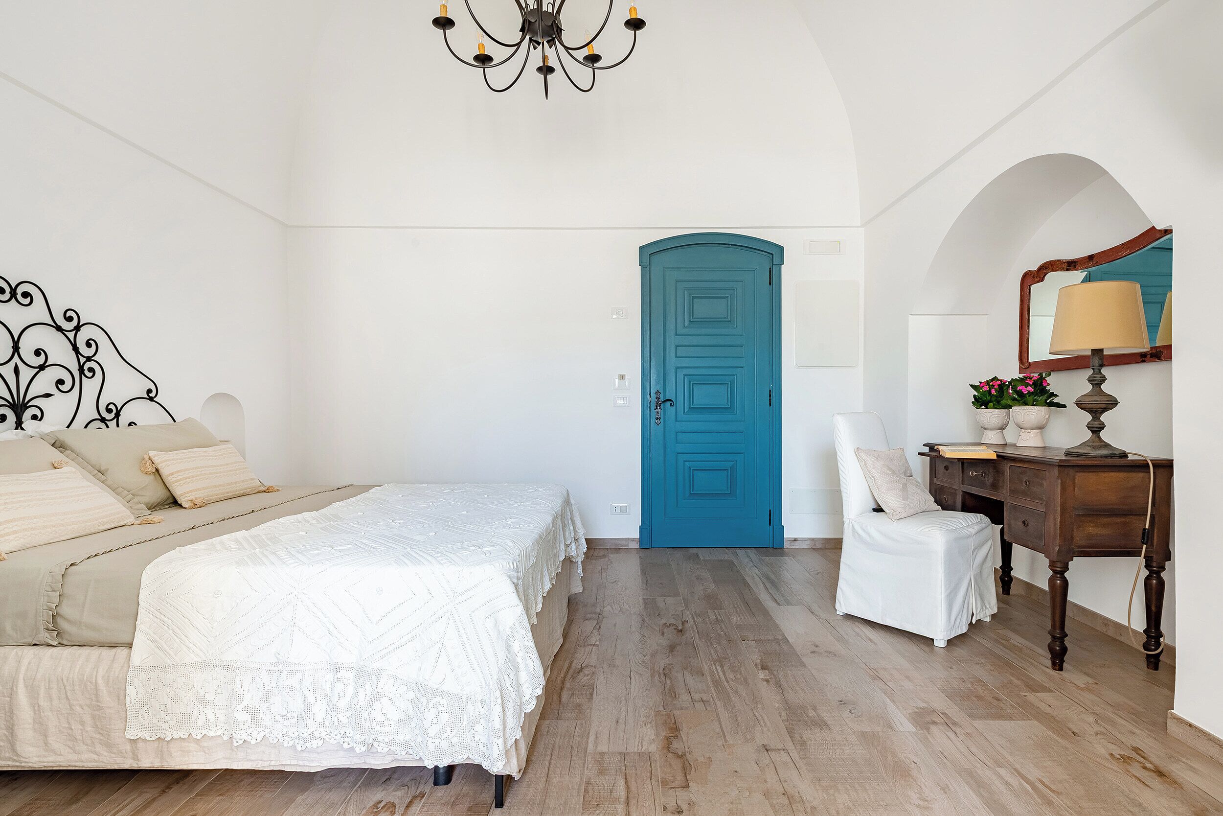 A bedroom with a bed, a blue door, a desk with a lamp, and a chair.