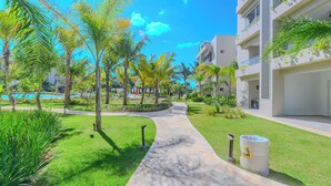 A pathway leading to a modern building with balconies, surrounded by lush greenery and a clear blue sky. - Vive Tracadero Lodge - 2 Hab Apto (Dominicus)