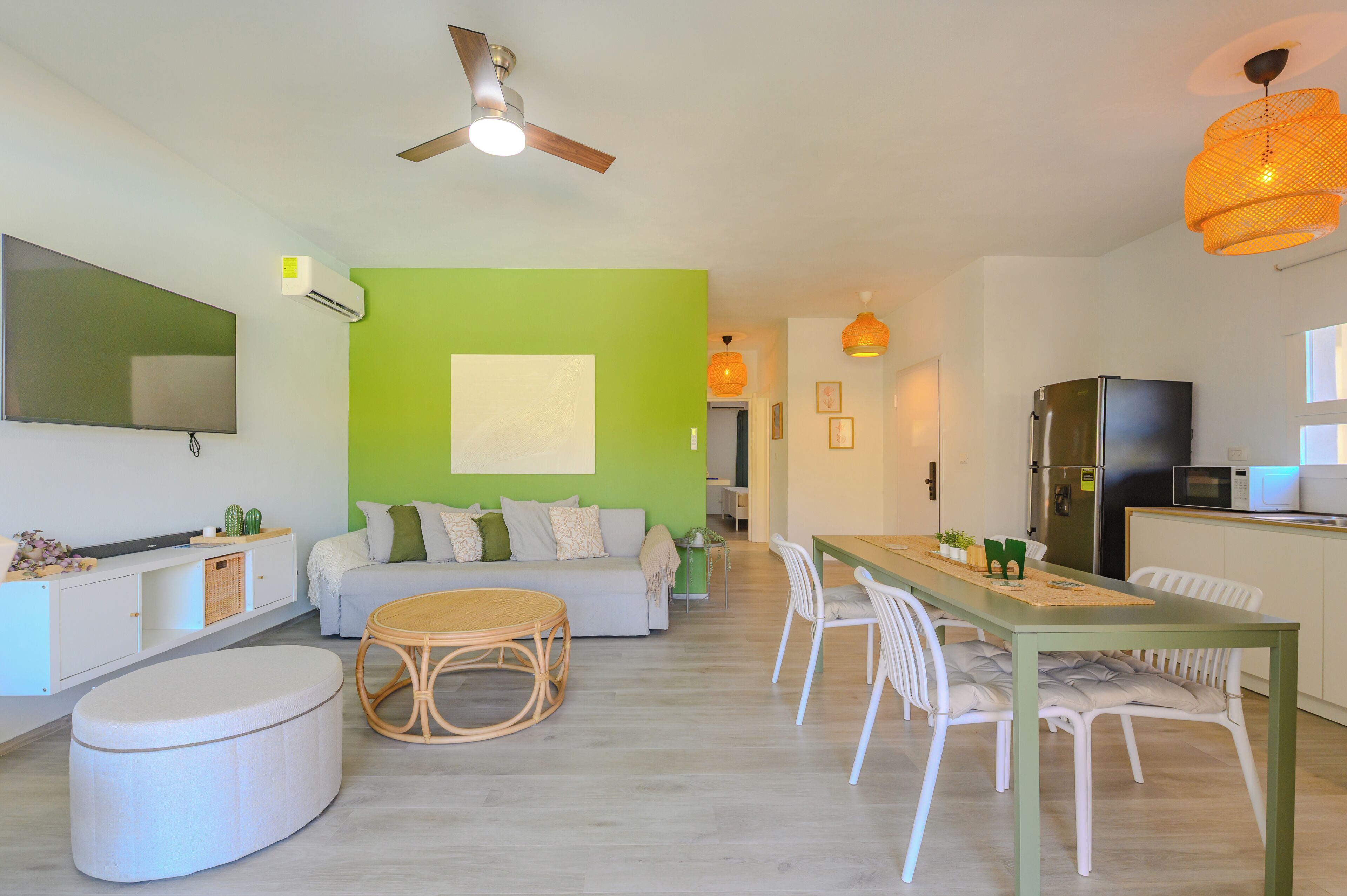 Ein modernes Wohnzimmer mit einer grünen Akzentwand, einem Essbereich mit weißen Stühlen, einem runden Holztisch und einem Deckenventilator.