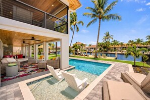 A poolside area with a hot tub, lounge chairs, and a view of a resort with palm trees and a pool. - NEW! Gorgeous Waterfront Pool Home, Outdoor BBQ Kitchen, 2 Large Patios & Dock (Marco Island)