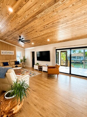 A spacious living room with a wooden ceiling, a large TV, and a view of a marina. - NEW! Gorgeous Waterfront Pool Home, Outdoor BBQ Kitchen, 2 Large Patios & Dock (Marco Island)