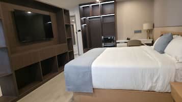 Una habitación de hotel moderna con una cama grande, un televisor de pantalla plana montado en la pared, un escritorio con lámpara y un armario con puertas correderas.