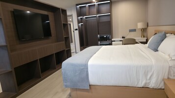 Una habitación de hotel moderna con una cama grande, un televisor de pantalla plana montado en la pared, un escritorio con lámpara y un armario con puertas correderas.