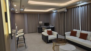 A modern hotel room with a sofa, armchairs, a desk, and a TV. - Plaza Court Hotel (Georgetown)