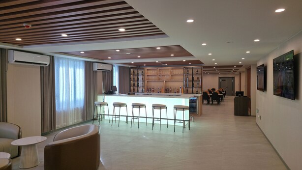 A modern hotel lobby with a bar area, seating, and a large TV screen. - Plaza Court Hotel (Georgetown)