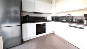 A modern kitchen with white cabinets, a stainless steel refrigerator, a built-in oven, and a dishwasher. - View of the Esterel massif from the Avant-Scene, Frejus on foot (Fréjus)