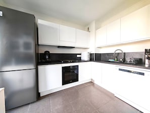 A modern kitchen with white cabinets, a stainless steel refrigerator, a built-in oven, and a dishwasher. - View of the Esterel massif from the Avant-Scene, Frejus on foot (Fréjus)