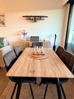 A wooden dining table with four chairs, a tray with glasses and snacks, a small table with a vase of flowers, a clock, and a speaker on a wooden cabinet. - View of the Esterel massif from the Avant-Scene, Frejus on foot (Fréjus)
