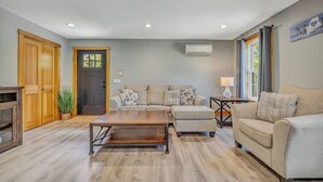 Sala de estar con sofá, reposapiés, mesa de centro, piso de madera y una puerta.