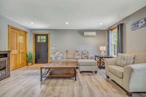 A living room with a sofa, ottoman, coffee table, wooden flooring, and a door.