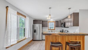 Una cocina moderna con una isla central, electrodomésticos de acero inoxidable, paneles de madera e iluminación colgante.