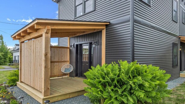 Une terrasse en bois avec une chaise, une porte et un jardin planté de fougères.