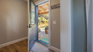 Un couloir avec une porte donnant sur un espace extérieur agrémenté de poutres en bois et de plantes en pot.
