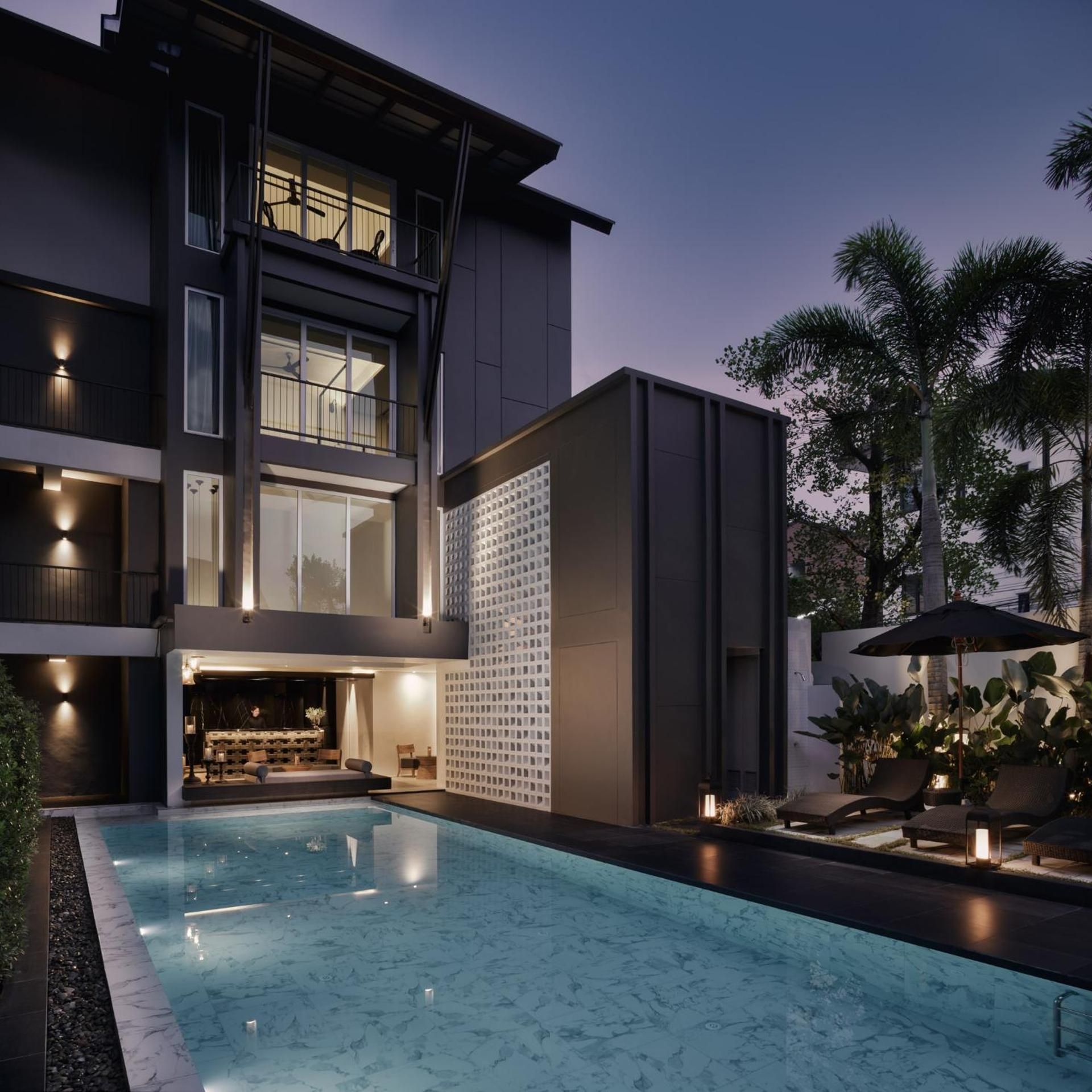 Un bâtiment moderne à deux étages, doté d’une piscine, d’un espace extérieur aménagé et d’une entrée bien éclairée.