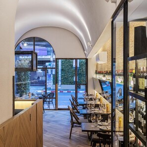 A restaurant with a modern interior, featuring a dining area with tables and chairs, a bar area with shelves of bottles, and large windows offering a view of the street outside. - Kiri Hotel Chiang Mai (Chiang Mai)