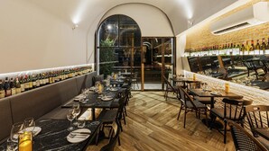 A restaurant interior with a long dining table, multiple chairs, a bar area with bottles, and a large arched window. - Kiri Hotel Chiang Mai (Chiang Mai)