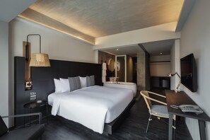Una habitación de hotel moderna con una cama grande, un escritorio, una silla, un televisor y un baño visible a través de una puerta abierta.