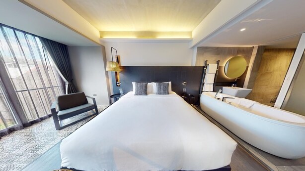 A modern hotel room with a large bed, a sofa, a bathtub, and a large window with curtains. - Kiri Hotel Chiang Mai (Chiang Mai)