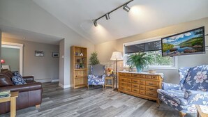 Uma sala de estar com um sofá de couro marrom, um armário de madeira, uma poltrona estampada e uma estante de livros.