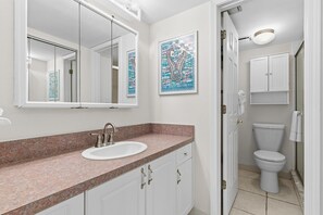 A bathroom with a white sink, a mirror, a toilet, and a shower area. - Pelican A403 (New Smyrna Beach)