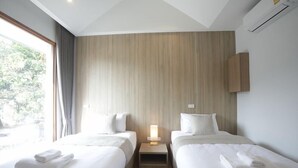 A hotel room with two beds, a nightstand with a lamp, and a view of greenery outside. - Four O'clock Hotel (Chiang Mai)