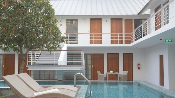 A modern indoor swimming pool with a lounge chair, wooden doors, and a staircase. - Four O'clock Hotel (Chiang Mai)