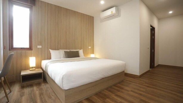 A modern bedroom with a wooden floor, a bed with white bedding, a nightstand with a lamp, and an air conditioning unit on the wall. - Four O'clock Hotel (Chiang Mai)
