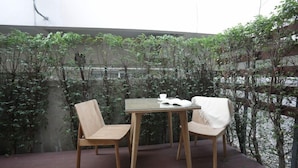 A wooden table with two chairs, a book, and a cup on it, set against a backdrop of greenery and a concrete wall. - Four O'clock Hotel (Chiang Mai)