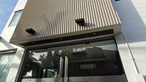 A modern building with a distinctive vertical wooden slat facade, large windows, and a clear sky. - Hotel De Wualai-sha Extra Plus (Chiang Mai)