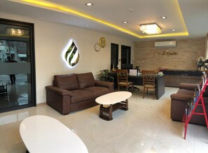 A modern living room with a brown sofa, a white coffee table, and a red magazine rack. - Hotel De Sripoom -sha Extra Plus (Chiang Mai)