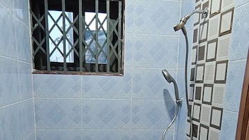 A small, tiled bathroom with a shower, a window with bars, and a patterned floor.