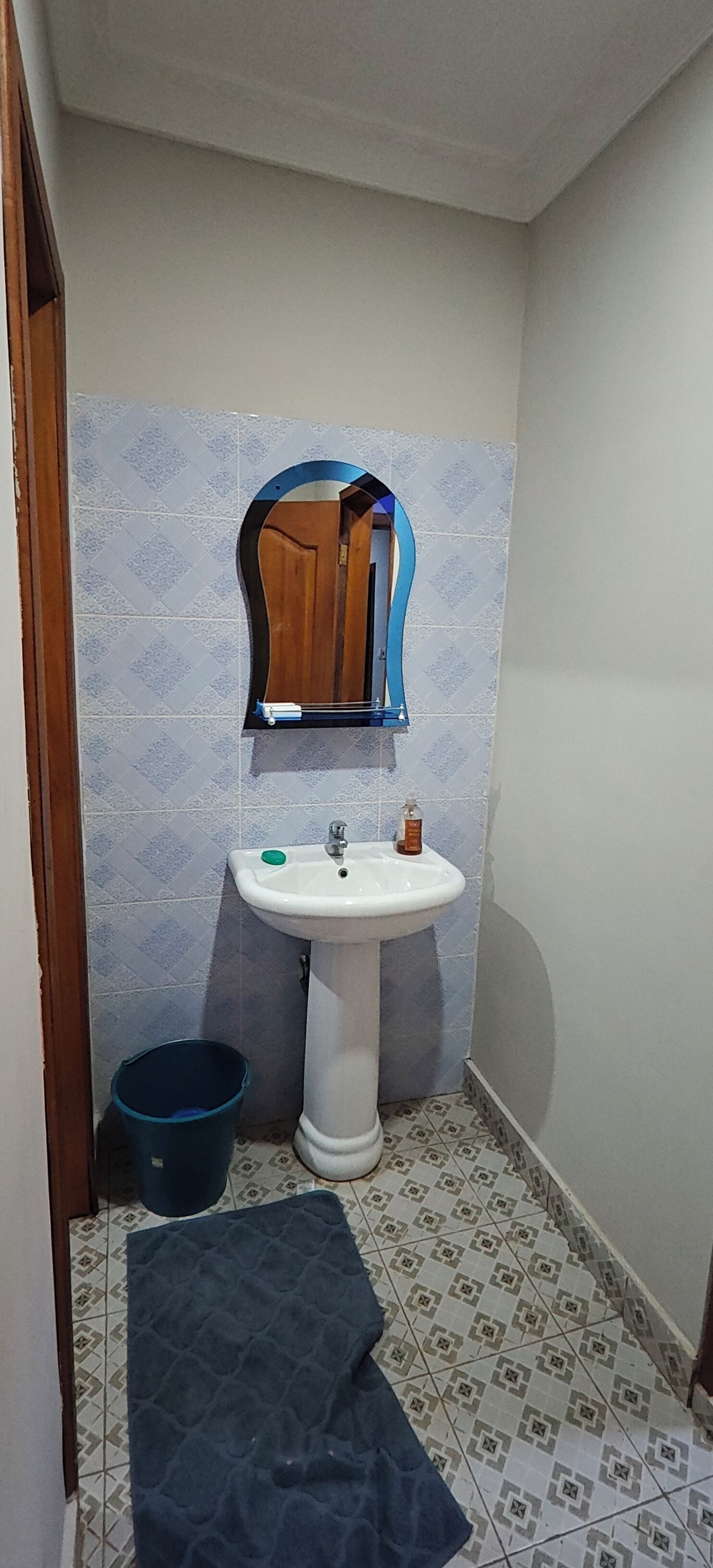 Ein kleines Badezimmer mit einem weißen Waschbecken, einem Spiegel und einer blauen Mülltonne.