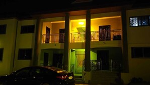 A two-story building with a balcony on the upper floor, a staircase leading to the entrance, and a parked car in front.