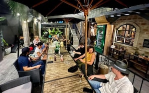 An indoor bar with wooden tables and chairs, a green vending machine, and a staircase leading to an upper level. - Book Design Hotel Sha Extra Plus (Chiang Mai)