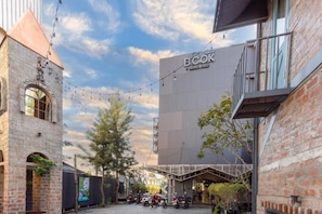 A courtyard with a modern building labeled 'BOOK HOTEL BY ISTY,' surrounded by brick structures and string lights. - Book Design Hotel Sha Extra Plus (Chiang Mai)