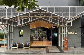 A modern building with a covered entrance, seating area with chairs and tables, and a sign indicating amenities. - Book Design Hotel -sha Extra Plus (Chiang Mai)