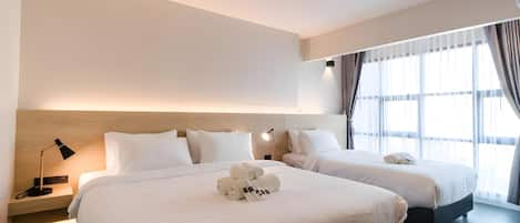 Habitación de hotel con dos camas, una mesita de noche con lámpara y un ventanal con cortinas.