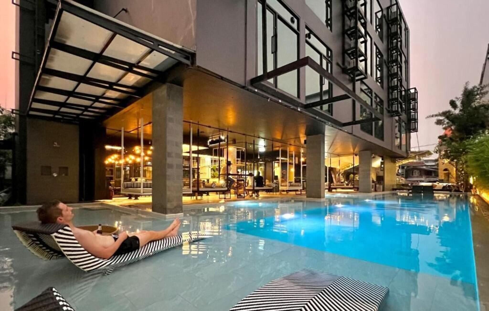 Zona de piscina con una persona recostada en una silla de descanso.