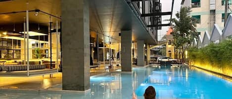 An indoor swimming pool with a person relaxing in a lounge chair.