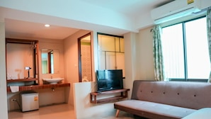 Une chambre d’hôtel avec un canapé, une télévision, un petit réfrigérateur, un lavabo et une fenêtre avec des rideaux.