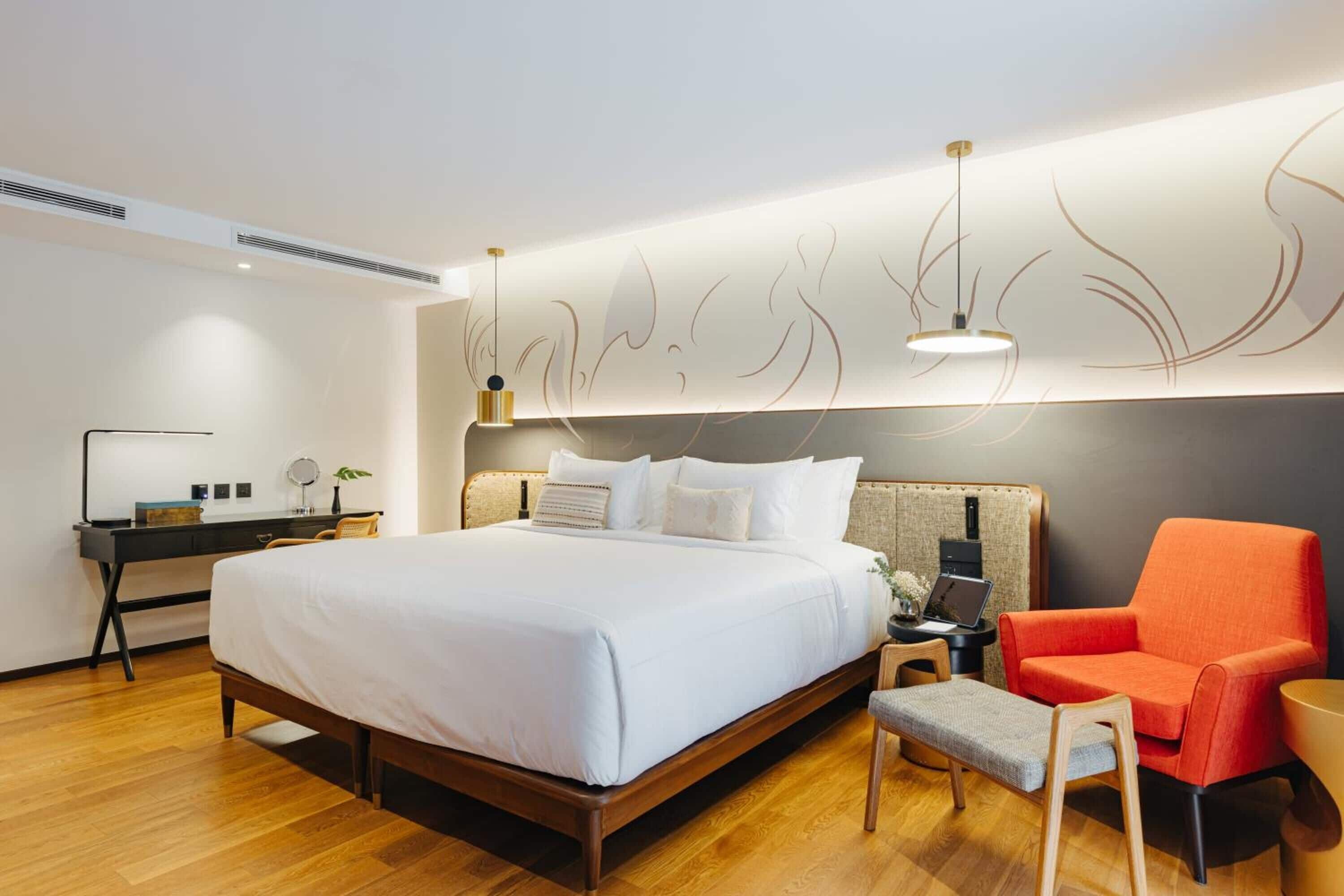 A modern hotel room with a large bed, a desk with a laptop, a chair, and a decorative wall panel.