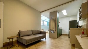 A modern, well-lit living room with a sofa, a small table, and a kitchen area with a refrigerator and cabinets. - Beachfront apartment, two suites, Post 9 - Ipanema (Rio de Janeiro)